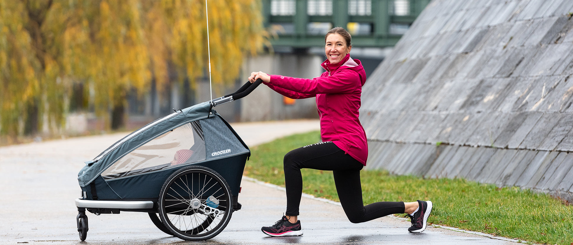 Woman in lunge exercise position holding Croozer bike trailer with safety flag during autumn workout